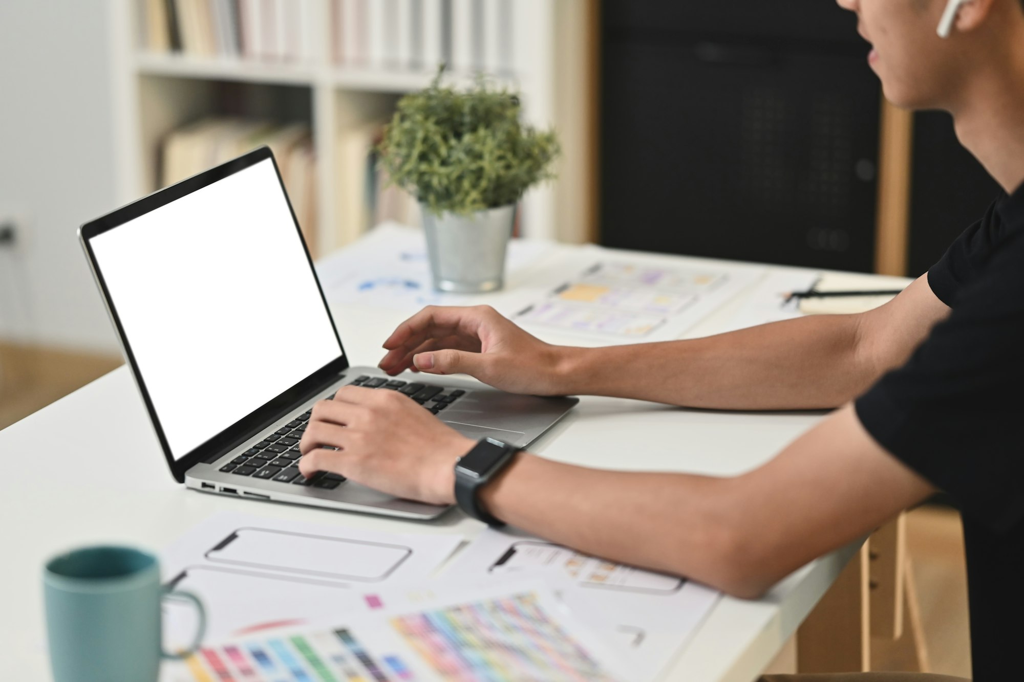 Cropped shot of male designer using laptop, working on mobile app development at modern workplace.